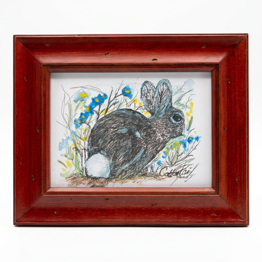 A 5x7 fine art wildlife print of a dark desert cottontail rabbit with a pale blue-white tail, drawn in ink and watercolor with blue flowers and green foliage, signed Gene Irvin. The artwork is displayed in a rustic cherry-red wood frame.